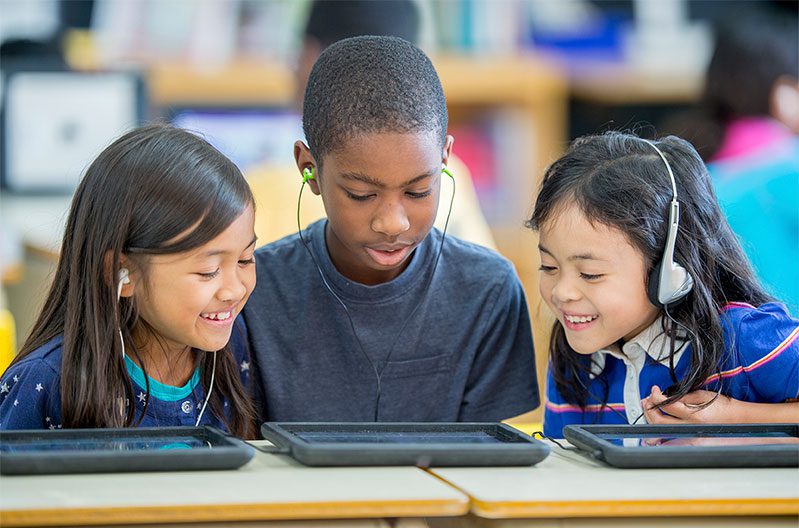 Young children learning and listening together on tablets in a classroom setting.